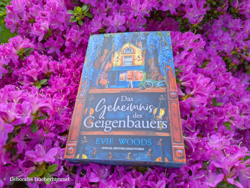 "Das Geheimnis des Geigenbauers" von Evie Woods umgeben von Blumen.